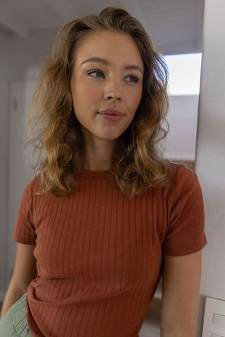Sunlit natural light portrait of young woman leaning by doorway in rust ribbed top