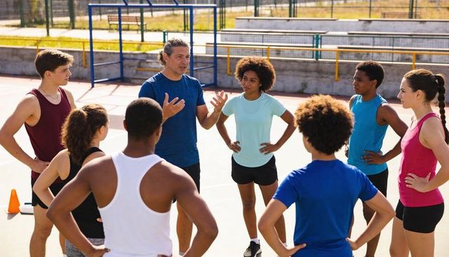Coach guiding diverse teen athletes during outdoor training huddle on sunlit court