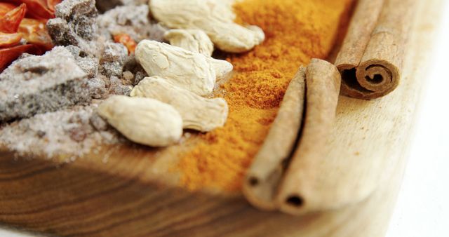 A variety of spices and herbs are arranged on a wooden surface, showcasing textures and colors that indicate culinary diversity. Cinnamon sticks add a warm, aromatic touch to the assortment, hinting at the flavors they can impart to dishes.