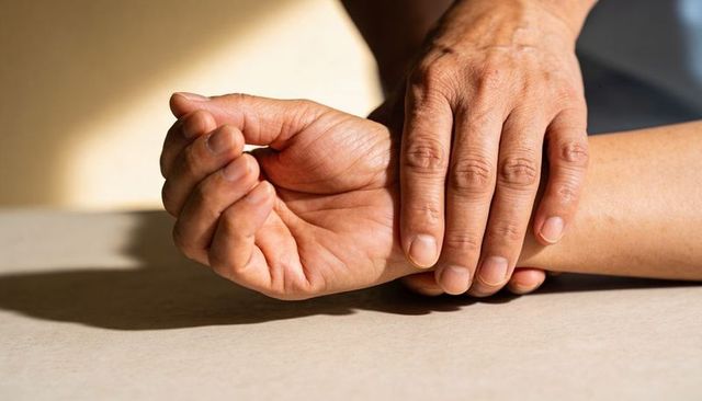 Senior hands showing veins and holding wrist gently on tabletop with warm natural light