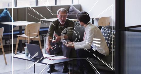 Male Colleagues Collaborating on Laptop and Documents in Modern Office Lounge for Project