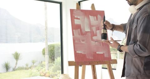 Indian artist painting abstract canvas in sunlit lakeside studio showing focused creativity