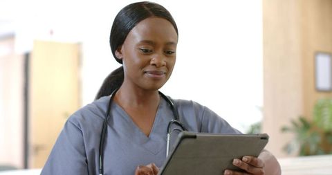 Nurse using tablet at clinic reception reviewing patient records and smiling
