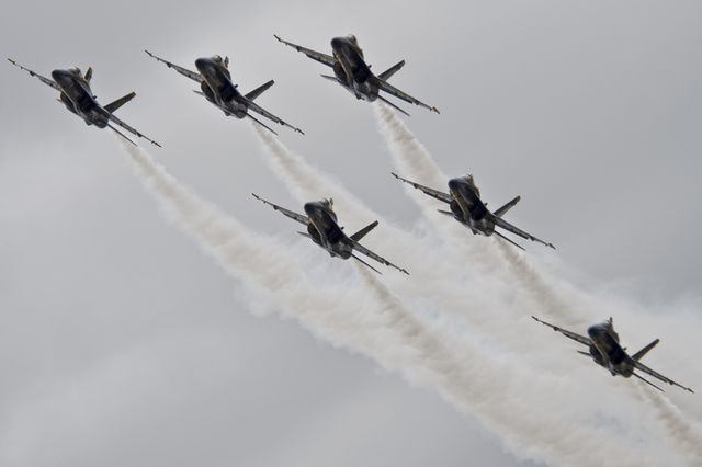 Jets performing synchronized movements in an airshow, leaving impressive smoke trails against a cloudy sky. Perfect for use in themes about aviation, air forces, teamwork, precision flying, aerobatics performances, and military displays.