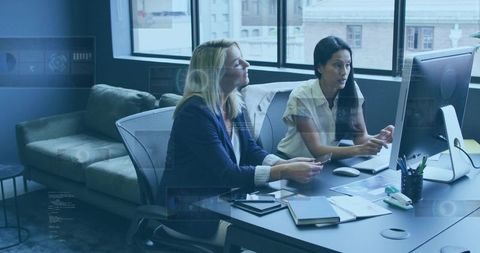 Businesswomen collaborating at desktop computer in modern urban office for teamwork