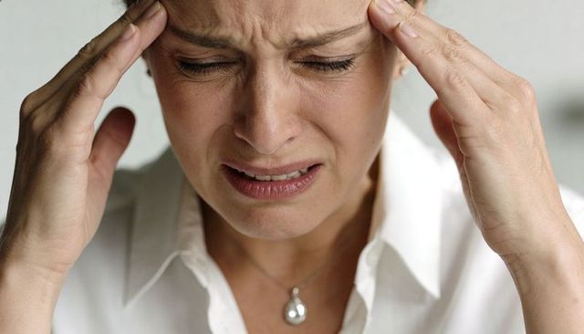 Middle-aged woman clutching temples, close-up portrait conveying headache and stress