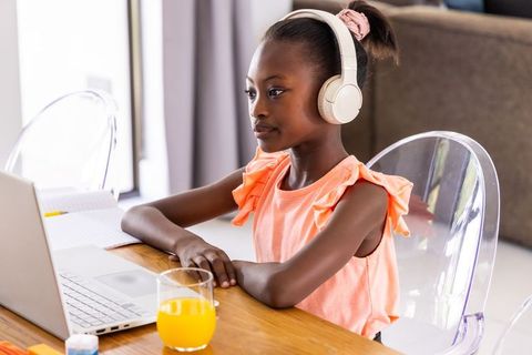 African girl studying at home with laptop and headphones, focusing on remote learning