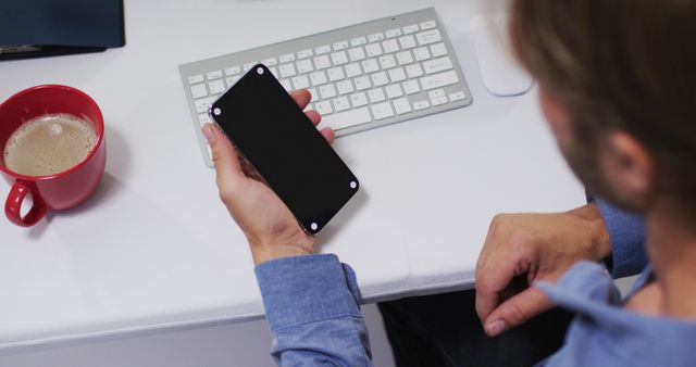 Man Working at Desk Holding Smartphone with Coffee - Download Free Stock Images Pikwizard.com