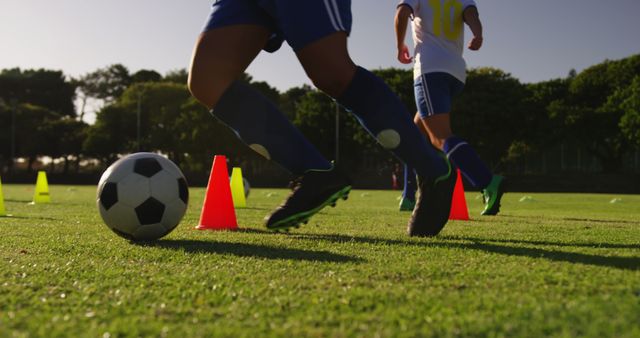 Children running soccer drills with colorful cones on a sunny, grassy field. Ideal for use in promoting youth sports programs, school physical education classes, coaching tutorials, fitness blogs, or advertisements for sports equipment.
