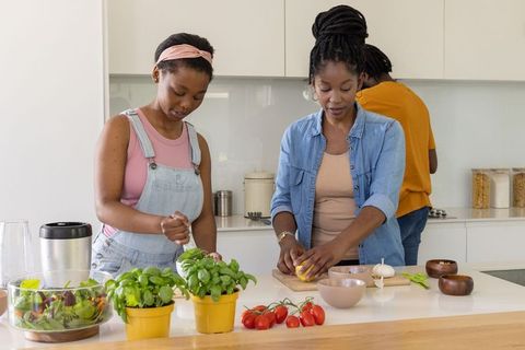 African family cooking together in modern kitchen preparing fresh salad, herbs, lemon