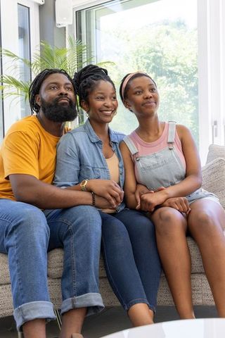 Family bonding on sofa holding hands, smiling parents with teenage daughter at home