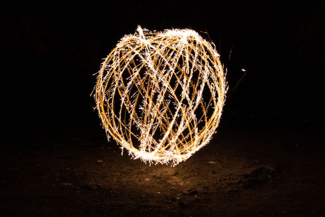 Creative representation of light painting using sparklers, showcasing long exposure technique to create a glowing orb in darkness. This abstract image is perfect for use in photography projects, event promotions, holiday themes, or creative design inspiration.