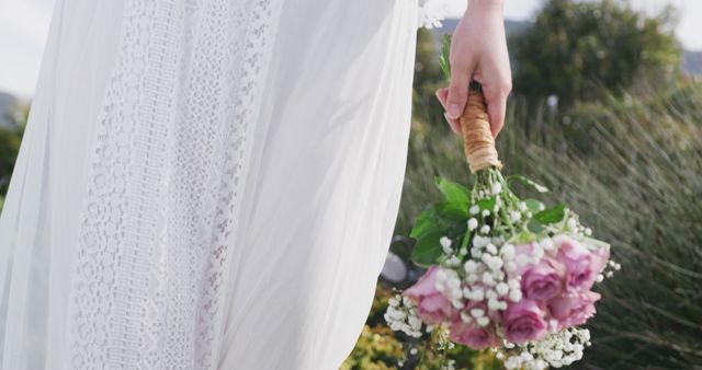 Image of mid section of bride in white dress walking holding bouquet at outdoor wedding. Marriage, love, happiness and inclusivity concept.