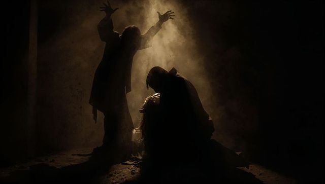 Cloaked figures looming over kneeling person in smoky cellar ritual spotlight