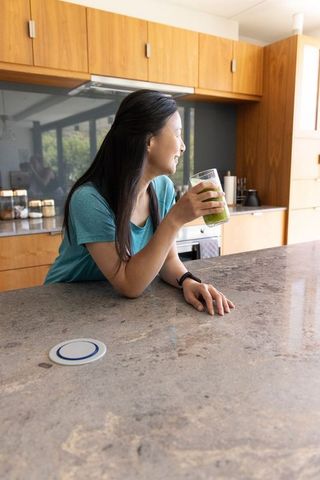 African woman leaning on kitchen island holding green smoothie morning wellness lifestyle