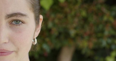Closeup young woman looking toward camera with silver hoop earring and soft foliage bokeh