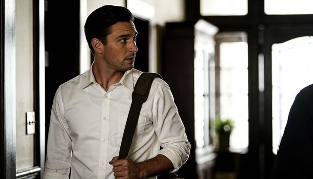 Young professional standing in sunlit foyer holding shoulder bag and looking right