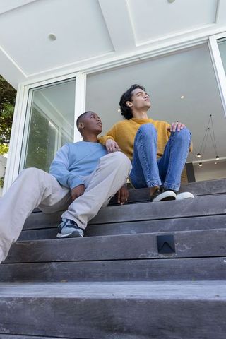 Two men sitting on modern wooden steps wearing sweaters and sneakers enjoying quiet moment