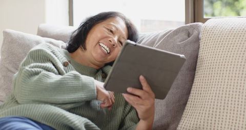Senior woman enjoying tablet on comfortable sofa at home