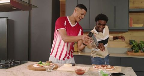 Two friends having fun making homemade pizza in spacious kitchen