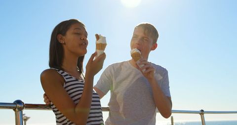 Joyful Young Couple Enjoying Ice Cream on a Sunny Seaside Promenade - Download Free Stock Images Pikwizard.com