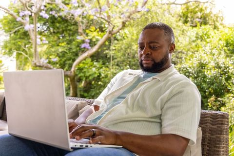 African american man working remotely on laptop in sunny garden patio