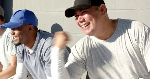 Smiling baseball teammates cheering on bench in sunny dugout celebrating victory, team spirit