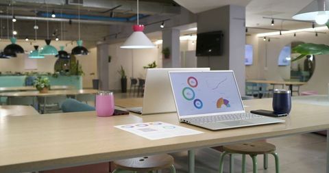 Silver laptop displaying colorful analytics dashboard on coworking table with tumblers