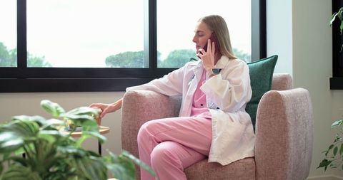 Female clinician in pink scrubs talking on smartphone reaching for cup in clinic lounge