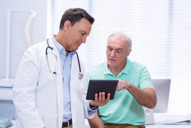 Doctor and senior patient using a digital tablet in a clinic. The doctor is wearing a white coat and the elderly man is pointing at the tablet. This image can be used for healthcare, medical consultations, patient care, and technology in medicine.