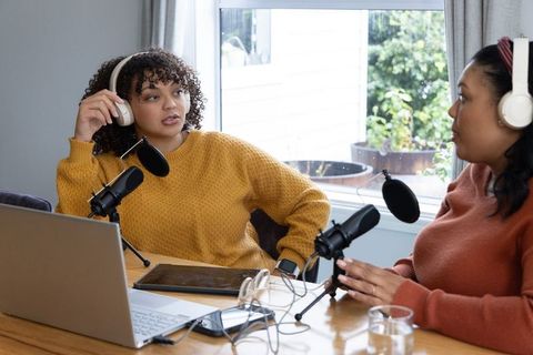 Diverse female podcast cohosts recording conversation in cozy home studio with microphones