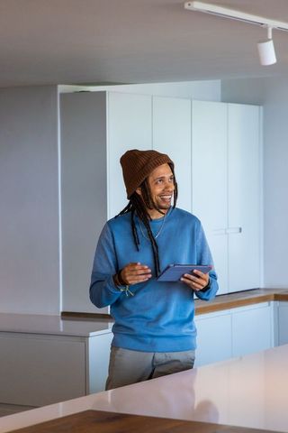 African american man standing at kitchen island holding tablet, gesturing, smiling