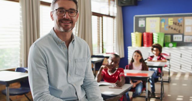 Portrait of happy caucasian male teacher in classroom with children looking at camera. children in primary school.