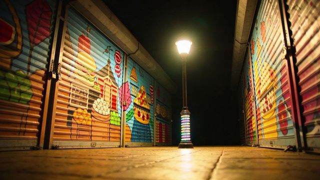 Low-angle night market lamppost illuminating colorful painted shutters and tiled walkway