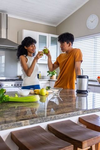 Diverse couple toasting fresh green juice at stone island after blending apple and celery