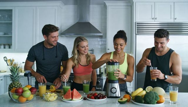 Fitness friends making green smoothies at kitchen island with fresh fruit and blender
