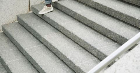 Person stepping down on urban concrete stairs wearing cuffed jeans and beige sneakers