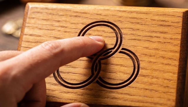 Finger tracing carved triple-ring puzzle on oak jewelry box, close-up wood grain texture