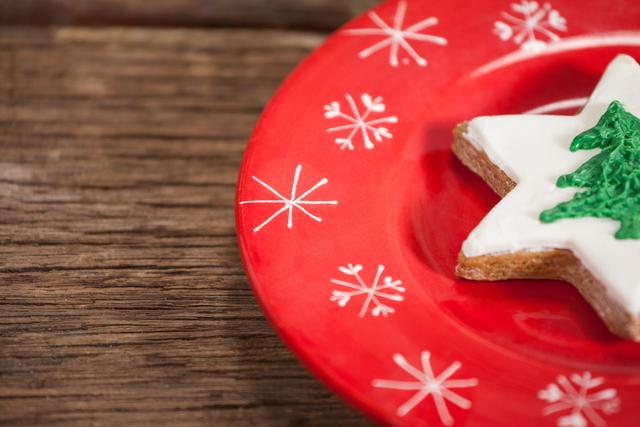Close-up of a star-shaped Christmas cookie with white icing and green tree decoration on a red plate with snowflake designs. Ideal for holiday-themed content, festive recipes, Christmas celebrations, and winter decorations.