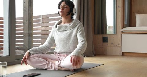 Woman Meditating with Headphones on Yoga Mat at Home