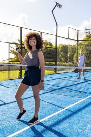 Young diverse women playing padel on vibrant blue court, smiling and posing with paddles