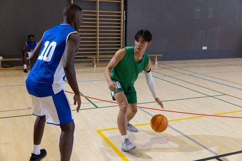 Young black and asian players dribbling and guarding on indoor basketball court, competitive play