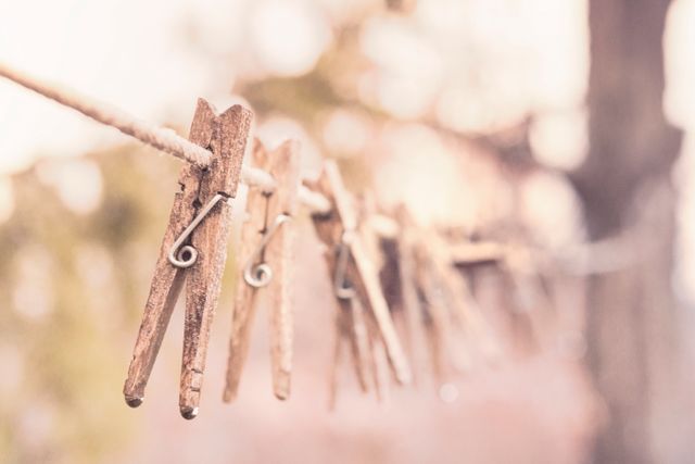 An array of wooden clothespins hanging on a rope line outdoors, evoking a rustic and vintage vibe. Ideal for themes of home, simplicity, traditional living, and domestic life. Can be used for blog posts, inspirational quotes, household articles, or advertisements that promote eco-friendly and sustainable living.