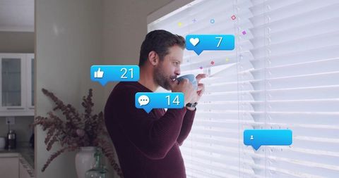 Sipping morning coffee while checking social notifications at window blinds