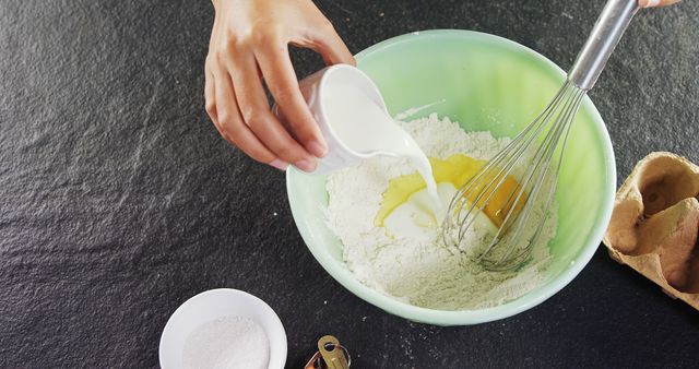 Close-up view of hands mixing flour, egg, and milk in bowl with whisk. Ideal for websites, blogs, and articles on cooking tutorials, homemade recipes, baking enthusiasts, and kitchen activities.