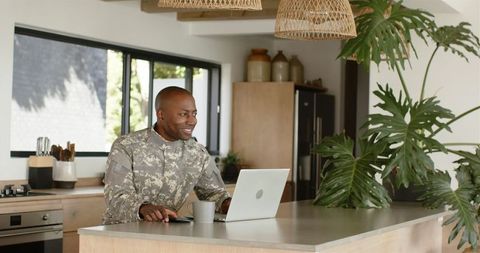Smiling Soldier Using Laptop and Smartphone in Modern Kitchen