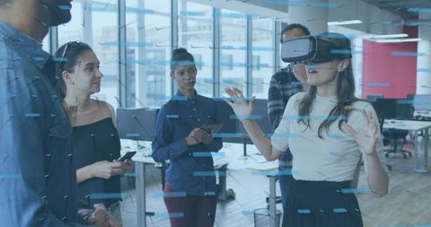 Woman Wearing VR Headset Gesturing as Team Observing Virtual Interface in Open-Plan Office
