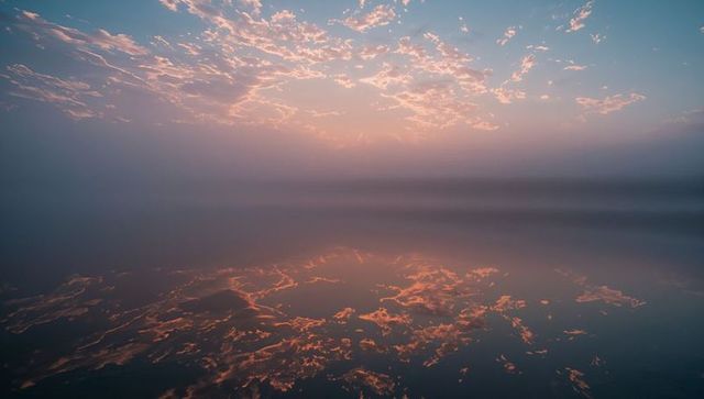Glowing Clouds Reflecting on Mirror-Flat Misty Lake at Dawn with Pastel Sunrise Glow