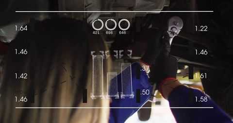 Female mechanic working under lifted car wearing gloves and blue coverall with HUD overlay