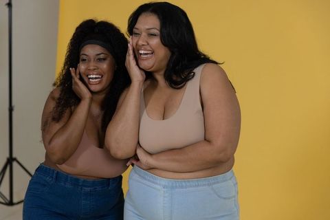 Diverse plus-size friends laughing and smiling on yellow backdrop in neutral tanks